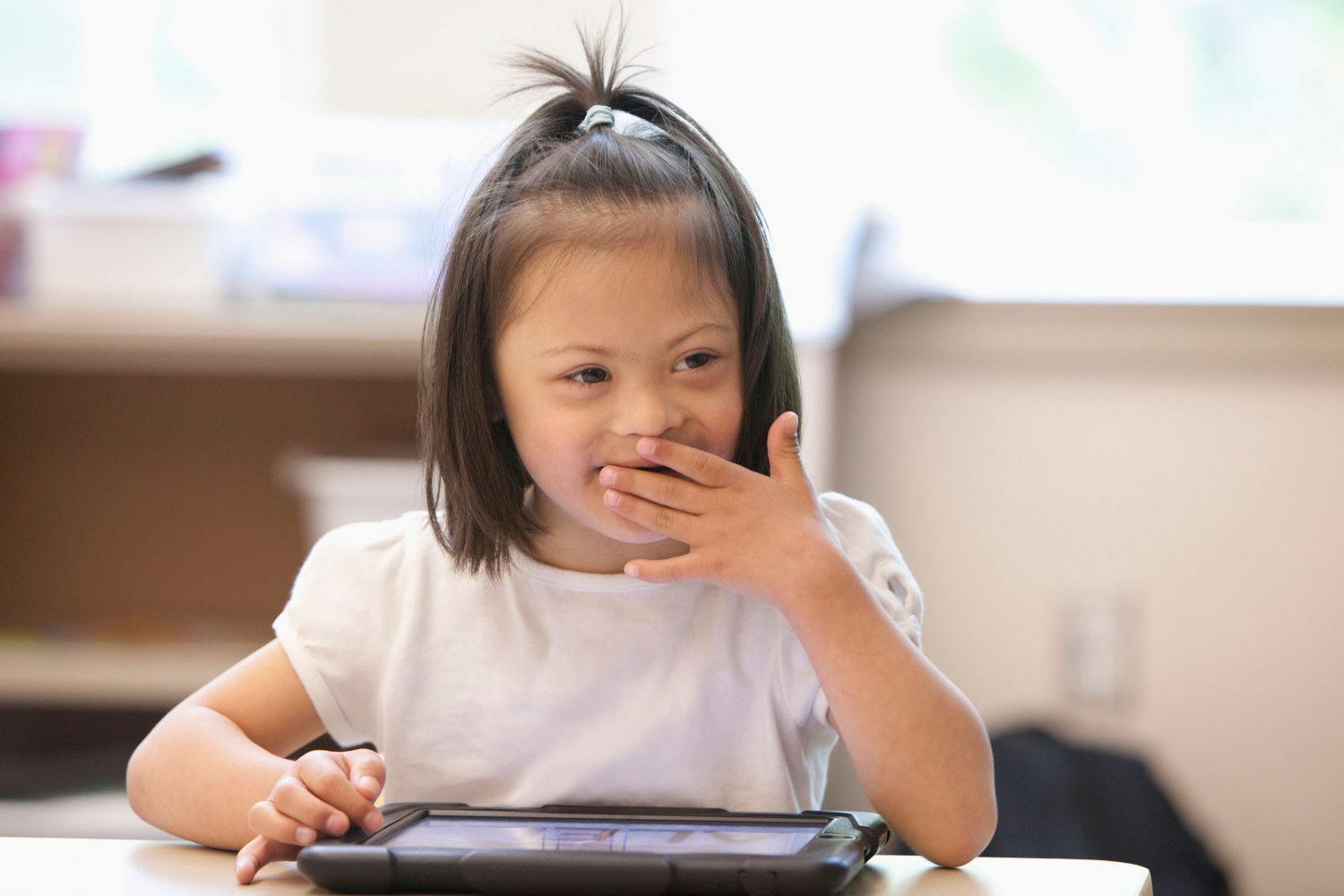 Asian girl with Down syndrome laughs while using a tablet