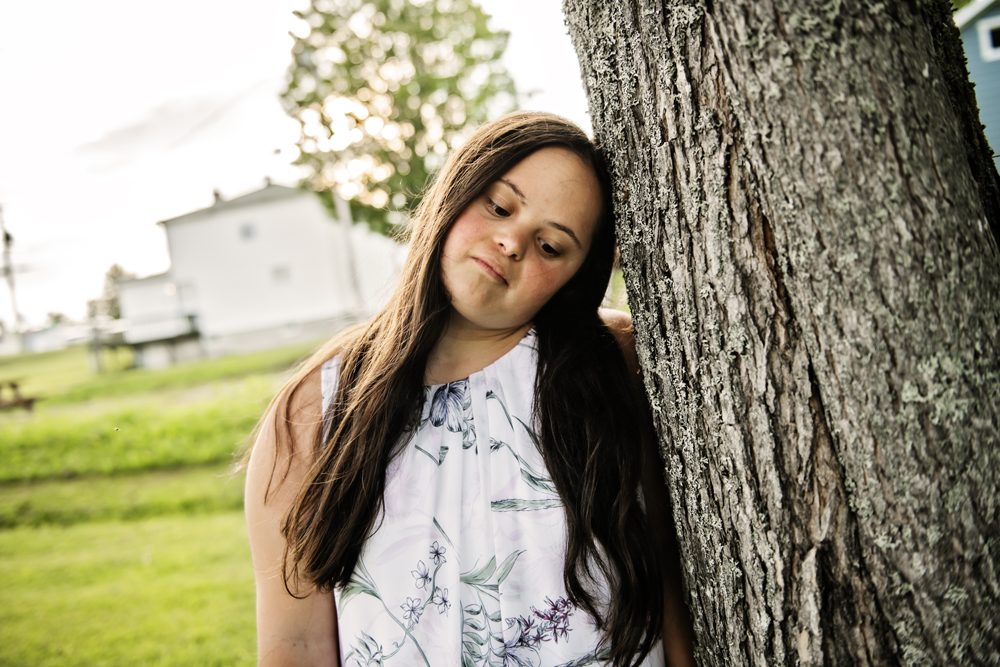 Sad woman with Down syndrome leans against tree