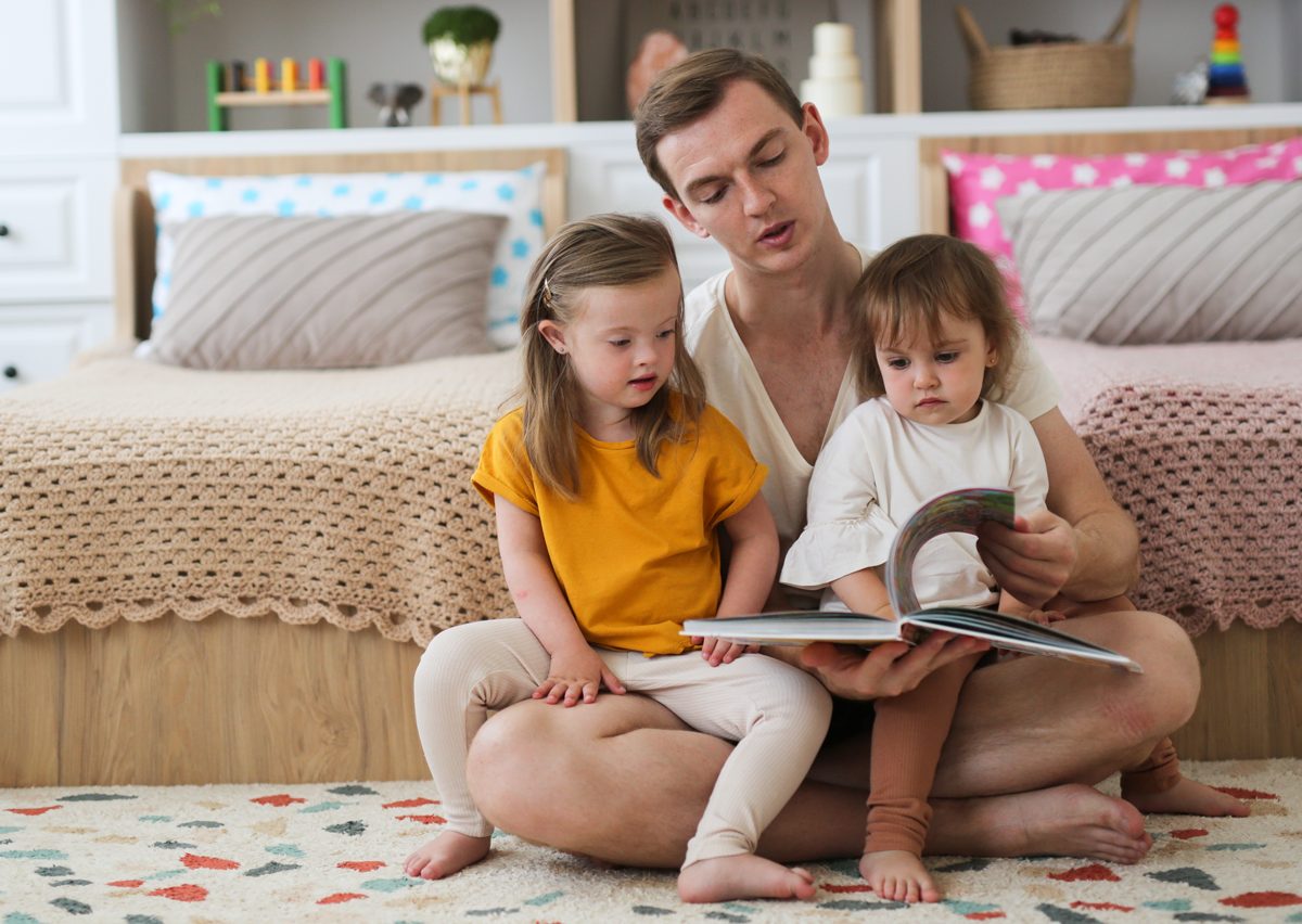 Man sits on floor reading to his two daughters