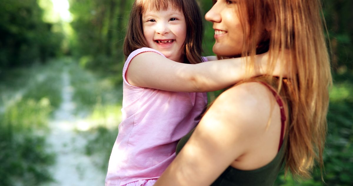 Mother carries daughter with Down syndrome down forest path