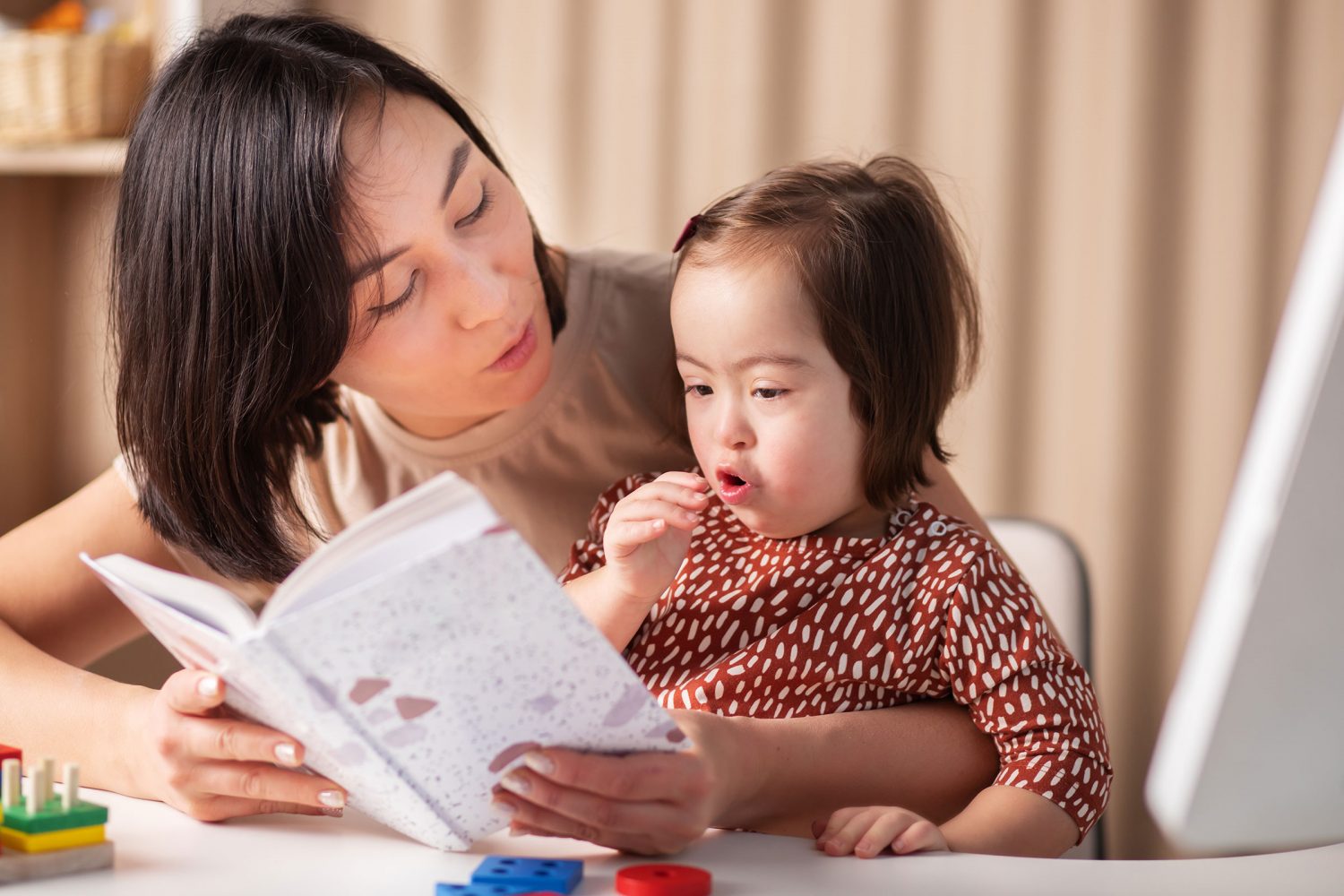 Asian mother reads book with her young daughter with Down syndrome
