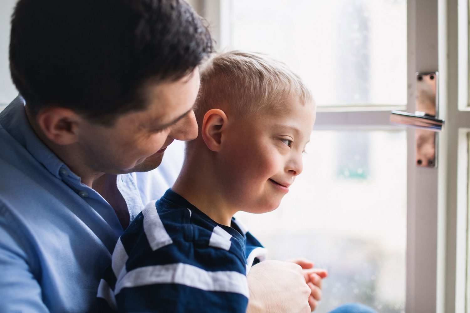 Father embraces his son with Down syndrome from behind