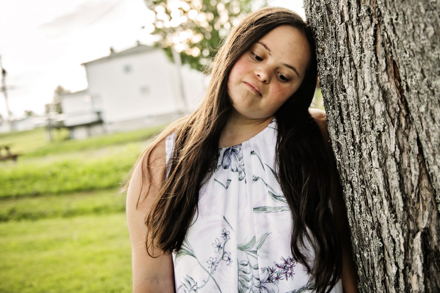 Sad young woman with Down syndrome leans against tree