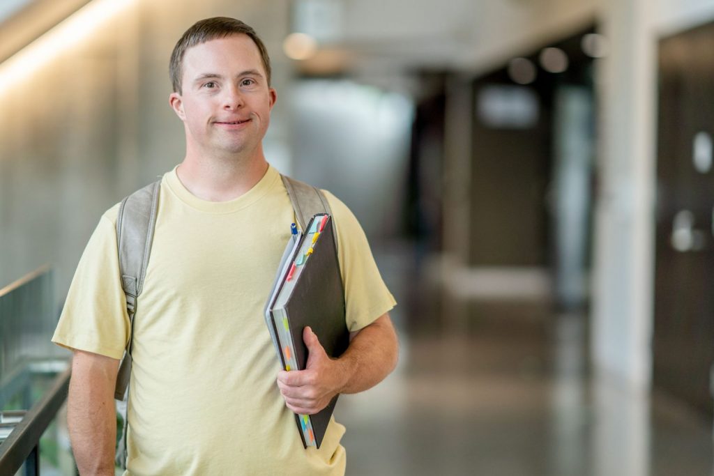 Young man with Down syndrome walks with book in school hallway