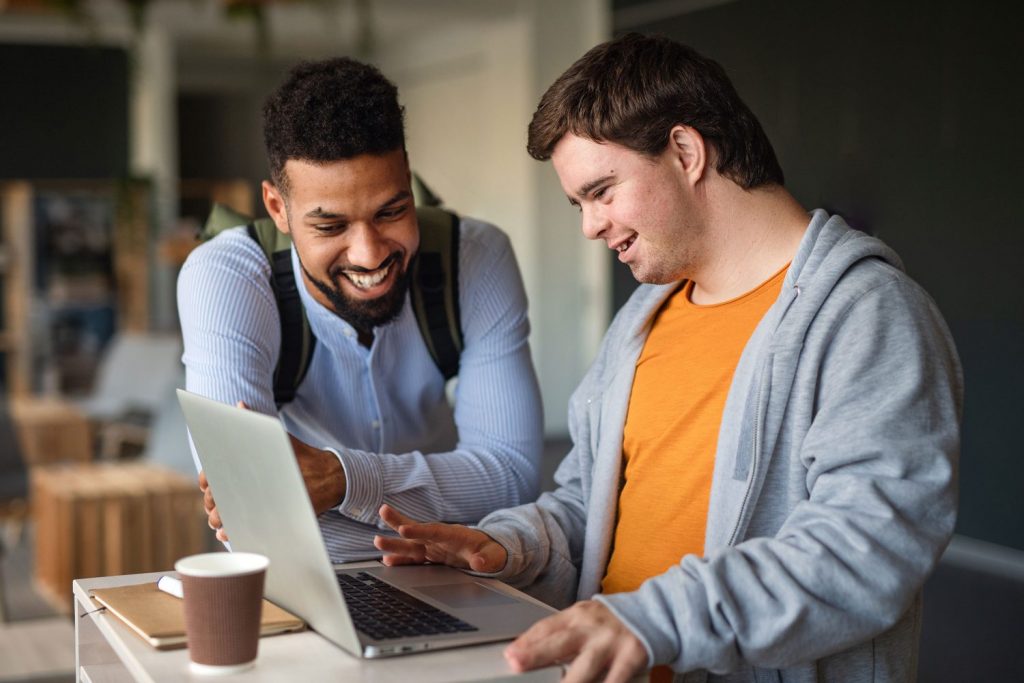 Young man with Down syndrome looks at laptop with his tutor