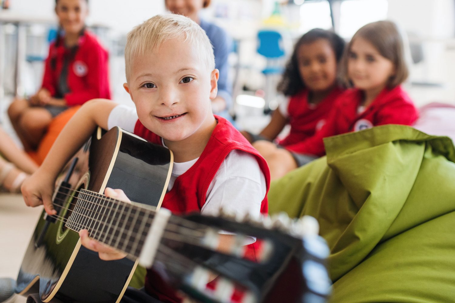 Boy with Down syndrome plays guitar as classmates look on