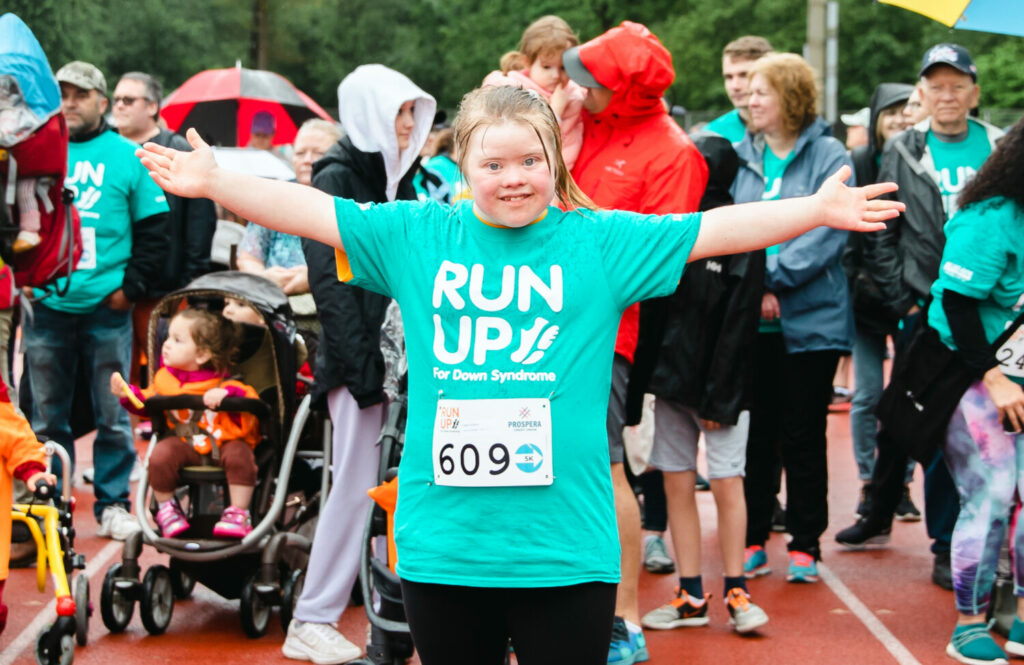 Teenage girl with Down syndrome wearing turquoise t-shirt stretches out arms in front of crowd