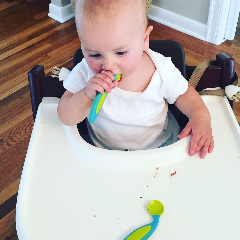 baby holding a spoon in his mouth, grasping near the scoop