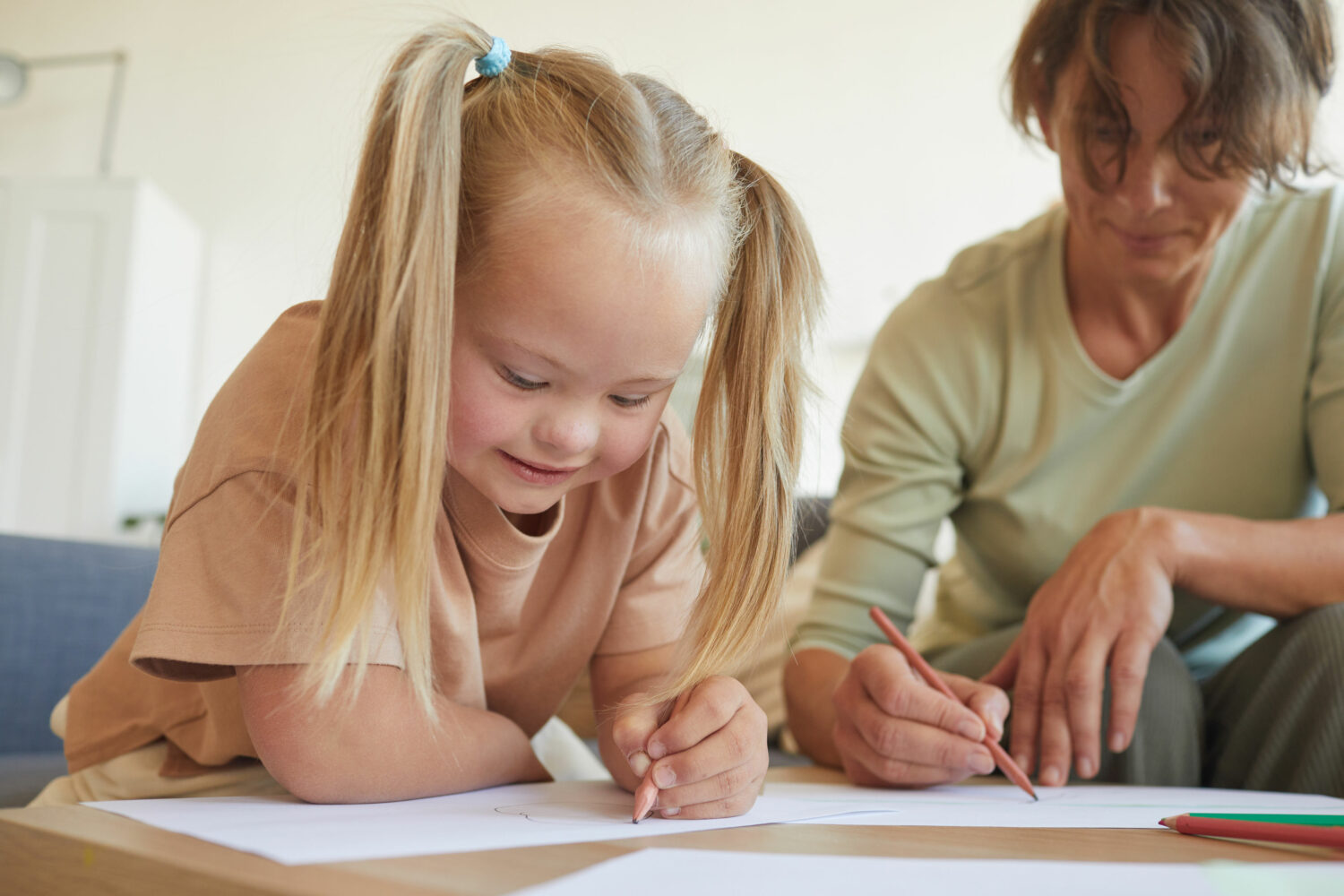 young blonde girl with Down syndrome works on school papers alongside teacher