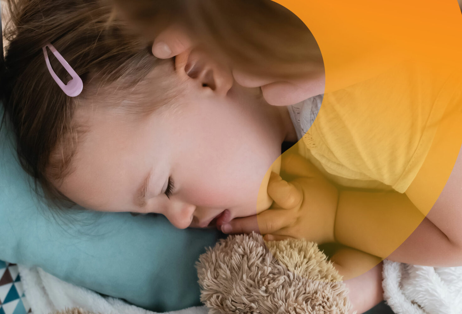 female toddler with Down syndrome sleeps on blue pillow, cuddling teddy bear