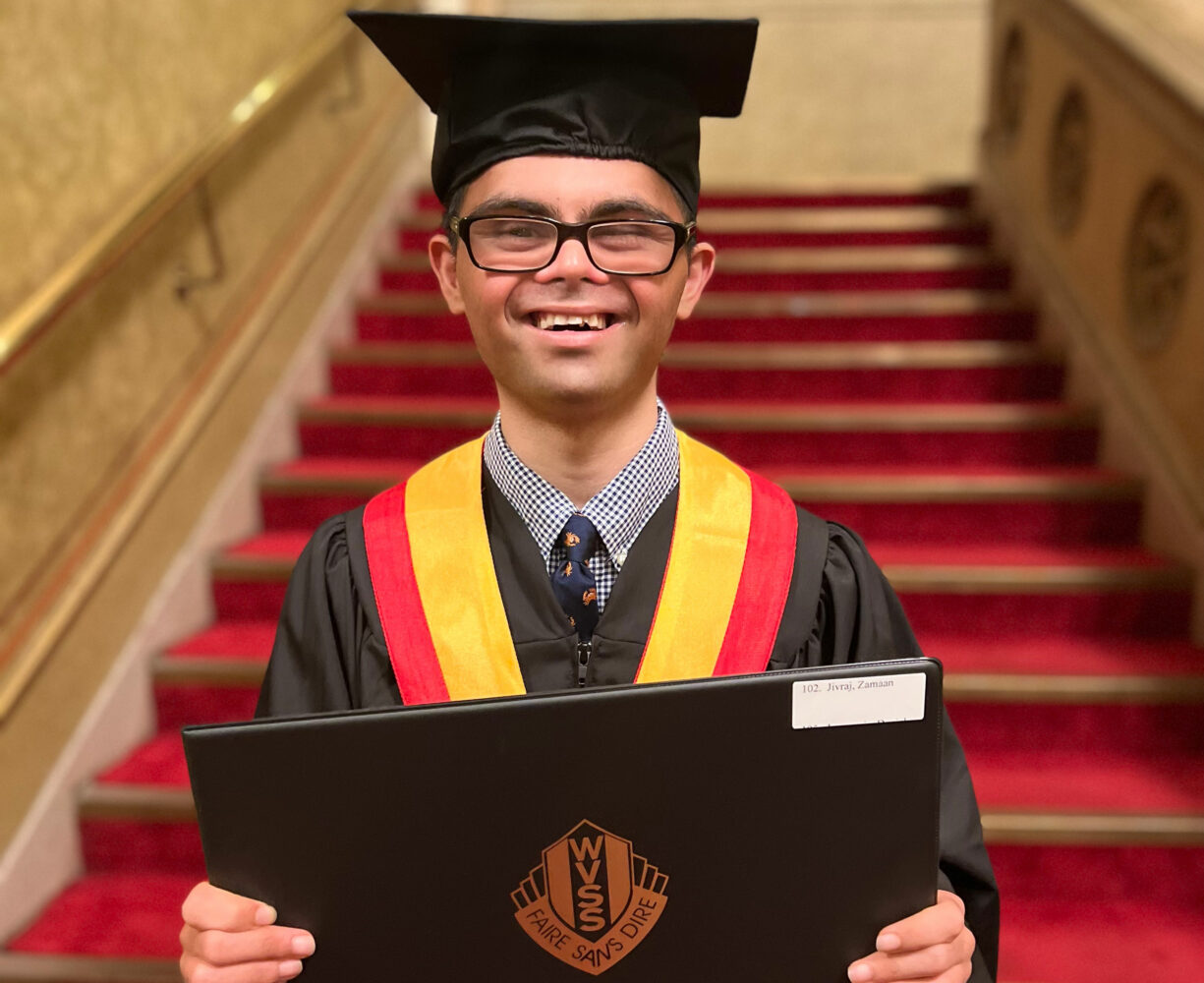 Asian teen with Down syndrome in graduation cap and gown, holding diploma