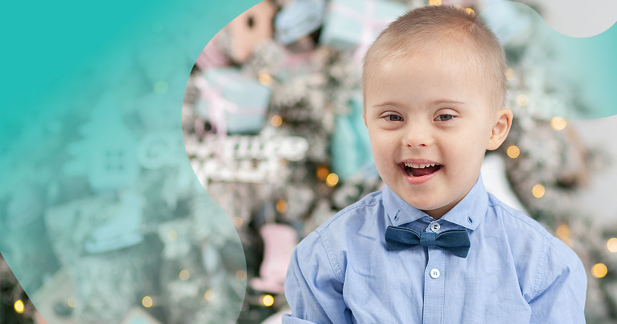young boy with Down syndrome wearing blue bowtie and blue dress shirt in front of Christmas tree