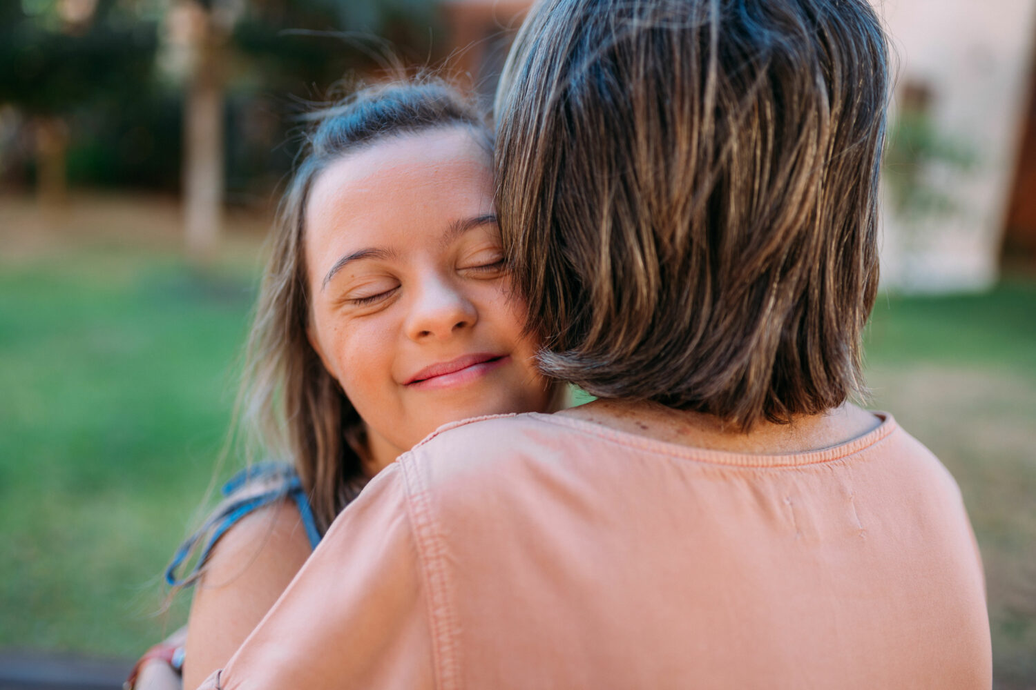 brown haired young woman with Down syndrome embraces her mother, pictured from over the mother's shoulder