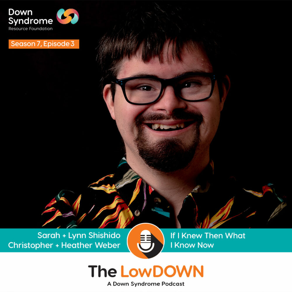 white man with Down syndrome, with dark hair, goatee and black glasses, smiles