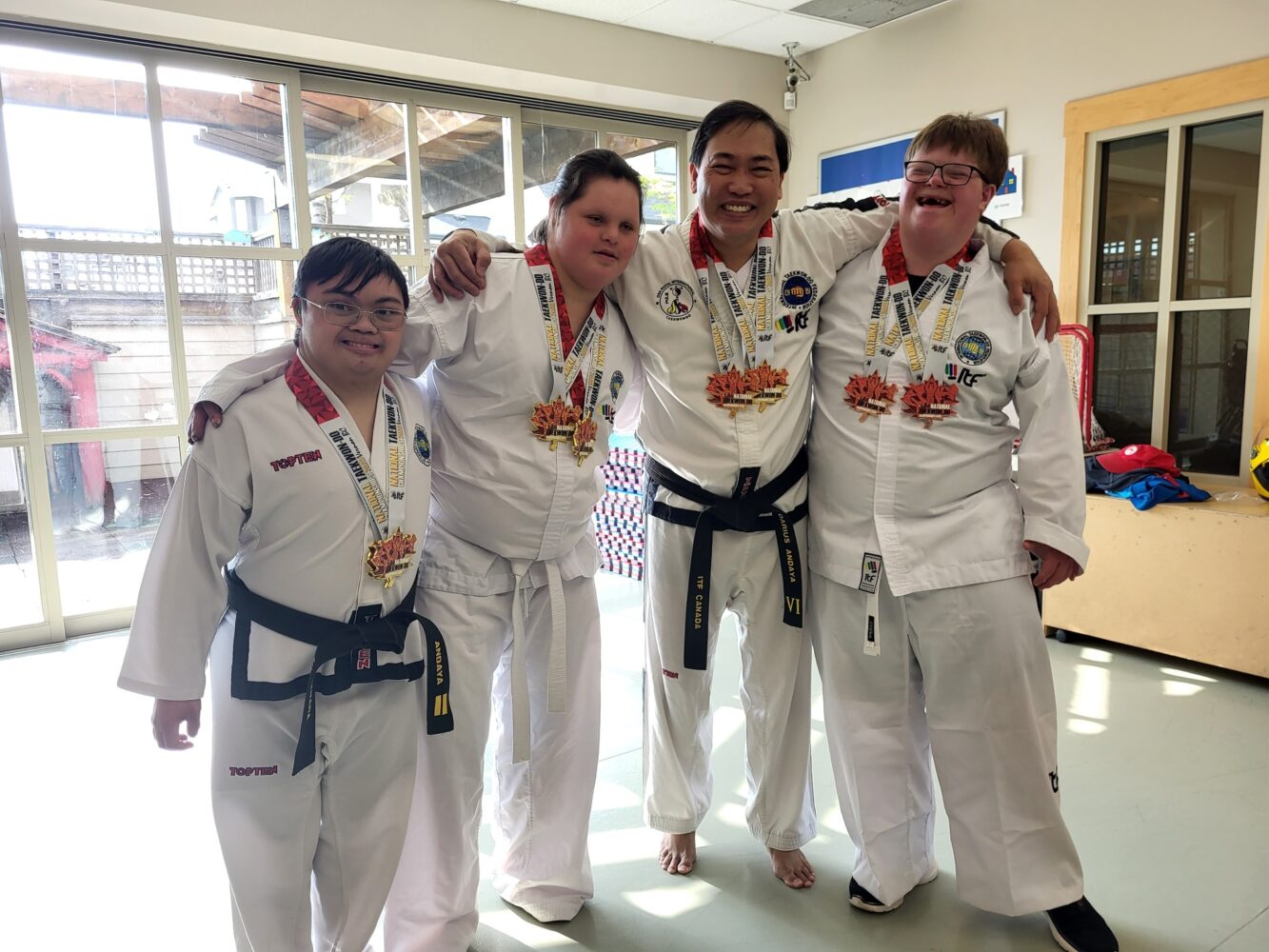 3 taekwondo students with Down syndrome pose with their instructor, all with Canadian championship medals around their necks