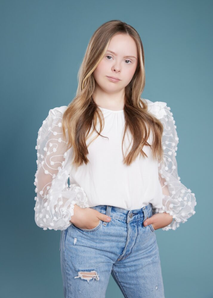 white female teenager with Down syndrome wearing white shirt with lace sleeves and blue jeans