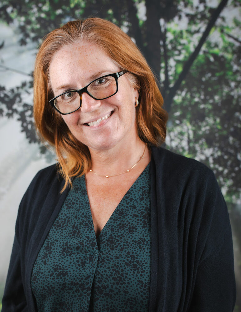 smiling white red headed woman wearing black glasses, green shirt and black sweater