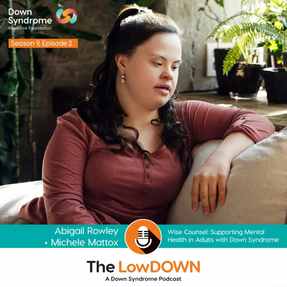 white woman with Down syndrome with long brown hair and burgundy long sleeve shirt sits on couch with arm draped over the cushion