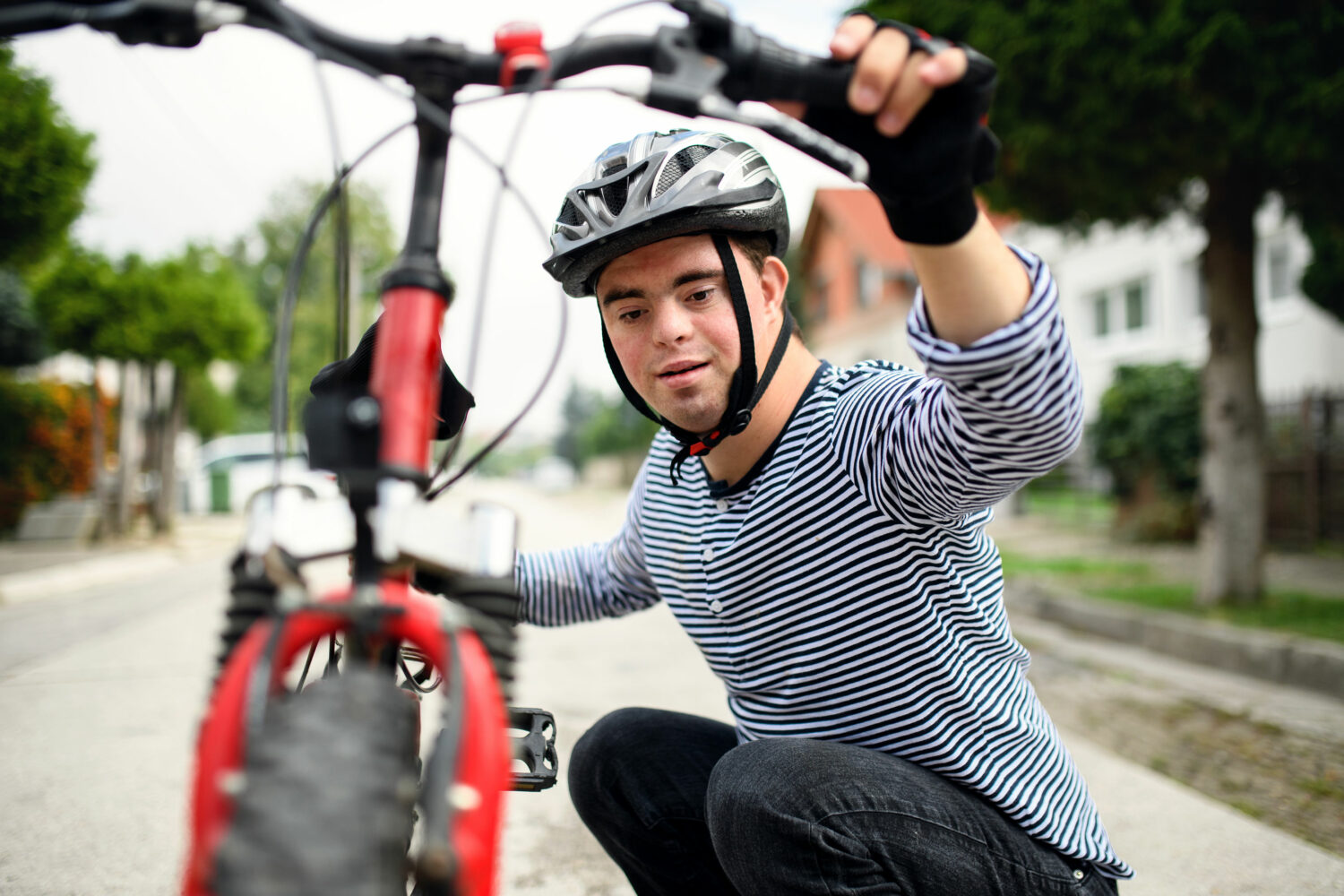 young white man with Down syndrome crouches down next to his bike