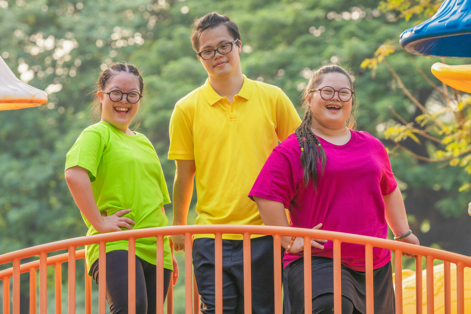 3 Asian young adults with Down syndrome stand together on playground bridge